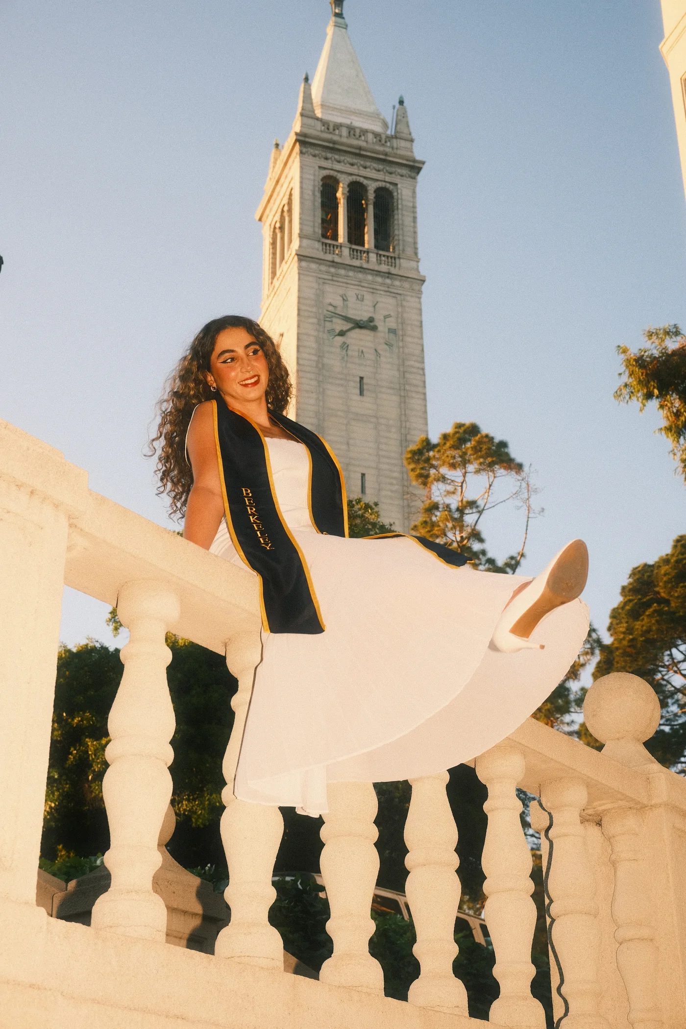 Graduation portrait on a balustrade below the Campanile at UC Berkeley, dress caught mid-turn in golden hour light