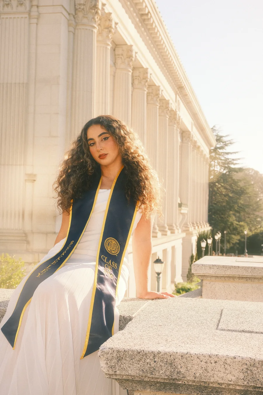 Graduation portrait seated against a colonnade, backlit by low sun